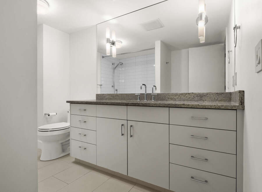 This modern bathroom features a sleek vanity with ample storage and a granite countertop, complemented by a stylish faucet.