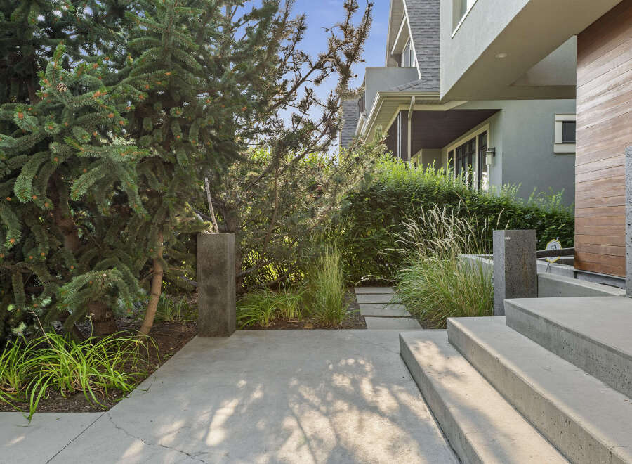 Modern concrete steps lead to the entrance of this stunning home, flanked by lush greenery and mature trees.