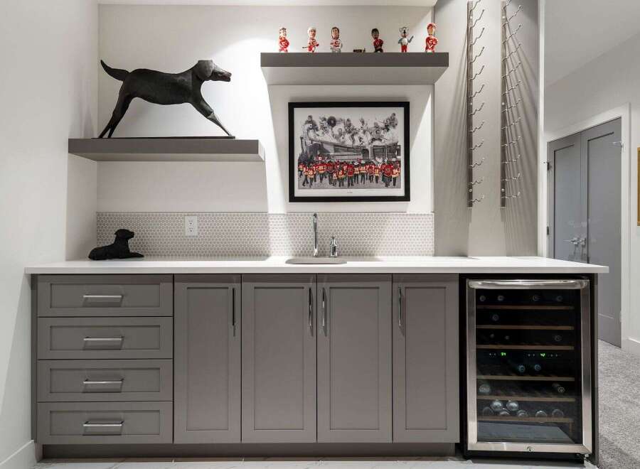 This modern wet bar features sleek grey cabinetry, a built-in wine fridge, and a stylish tiled backsplash.