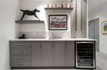 This modern wet bar features sleek grey cabinetry, a built-in wine fridge, and a stylish tiled backsplash.