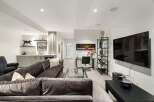 This modern basement living area features a spacious sectional sofa, a sleek wet bar with ample cabinetry, and a dedicated workspace with a glass-top desk.