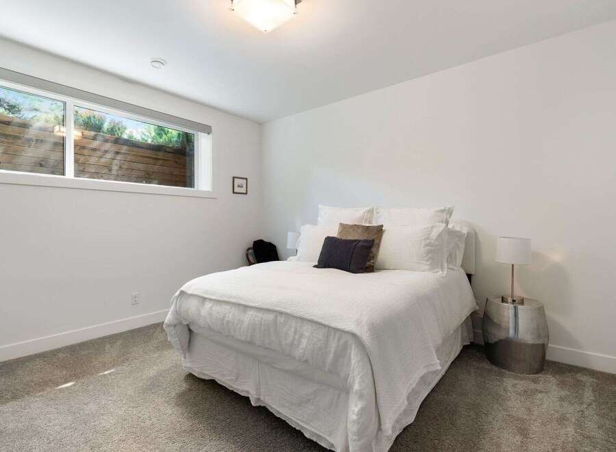 This modern bedroom features a comfortable queen-size bed with crisp white linens, complemented by a dark accent pillow and a textured throw.