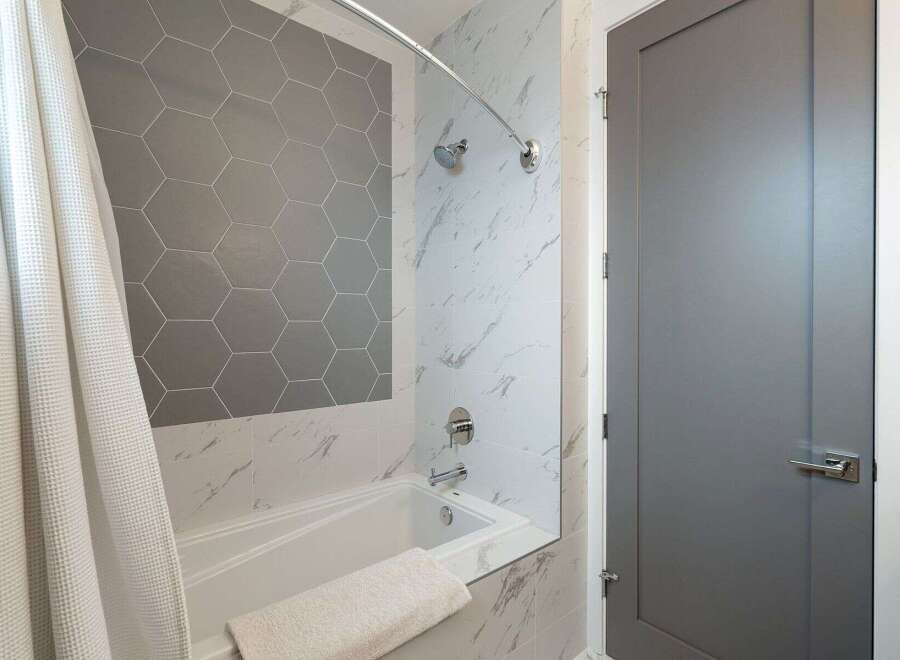 Experience modern luxury in this bathroom, featuring a sleek bathtub surrounded by elegant marble-patterned tiles.