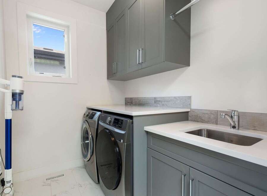 This modern laundry room features a sleek grey cabinetry setup with ample storage, including overhead cabinets and a spacious countertop.