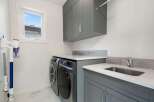 This modern laundry room features a sleek grey cabinetry setup with ample storage, including overhead cabinets and a spacious countertop.