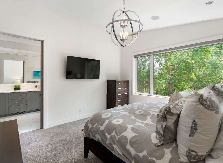 Experience modern comfort in this beautifully appointed bedroom, featuring a large window with lush green views and a stylish geometric chandelier.