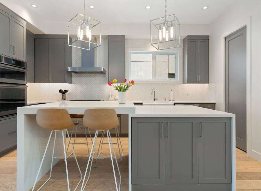 Experience modern luxury in this stunning kitchen, featuring sleek grey cabinetry, a spacious quartz island with seating, and a striking geometric pendant light.