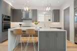 Experience modern luxury in this stunning kitchen, featuring sleek grey cabinetry, a spacious quartz island with seating, and a striking geometric pendant light.