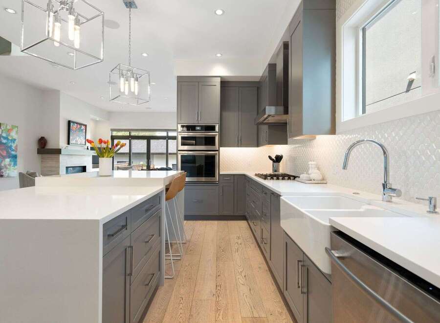 Experience modern luxury in this stunning kitchen, featuring sleek grey cabinetry, a large island with a white quartz countertop, and a farmhouse sink.