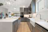 Experience modern luxury in this stunning kitchen, featuring sleek grey cabinetry, a large island with a white quartz countertop, and a farmhouse sink.