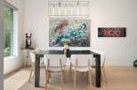 This elegant dining room features a large abstract painting above a dark wood dining table, complemented by modern white chairs.