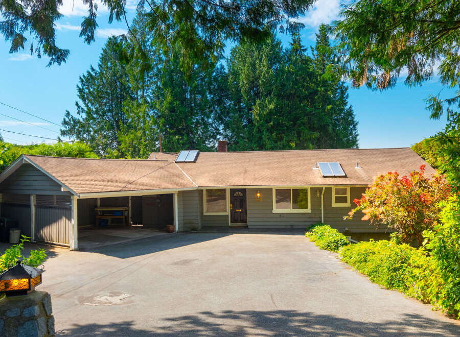 Charming single-story home with a covered carport and a spacious driveway, nestled amidst lush greenery and mature trees.