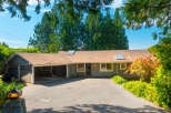 Charming single-story home with a covered carport and a spacious driveway, nestled amidst lush greenery and mature trees.