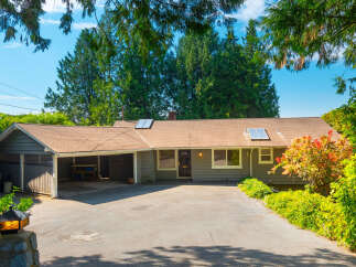 Charming single-story home with a covered carport and a spacious driveway, nestled amidst lush greenery and mature trees.
