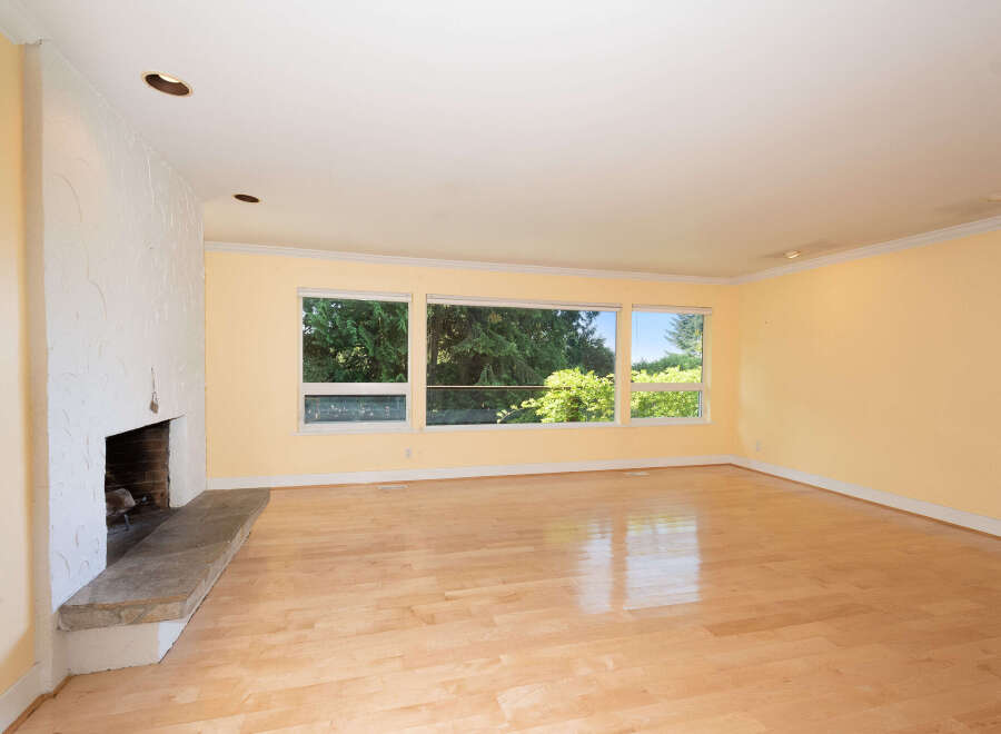 Experience the warmth and natural light in this spacious living area, featuring a striking textured fireplace and expansive windows that offer a beautiful view of the lush greenery outside.