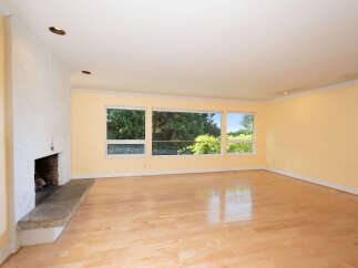 Experience the warmth and natural light in this spacious living area, featuring a striking textured fireplace and expansive windows that offer a beautiful view of the lush greenery outside.