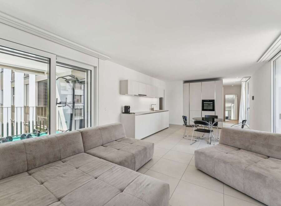 Experience modern living in this bright and airy open-concept apartment, featuring a sleek white kitchen with integrated appliances and ample counter space.