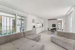 Experience modern living in this bright and airy open-concept apartment, featuring a sleek white kitchen with integrated appliances and ample counter space.