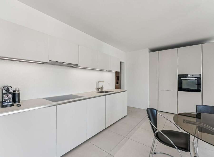 Experience modern living in this sleek, white kitchen featuring integrated appliances and ample cabinet space.