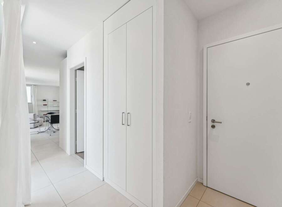 Step into this bright and airy hallway, featuring sleek white walls and a pristine tiled floor.