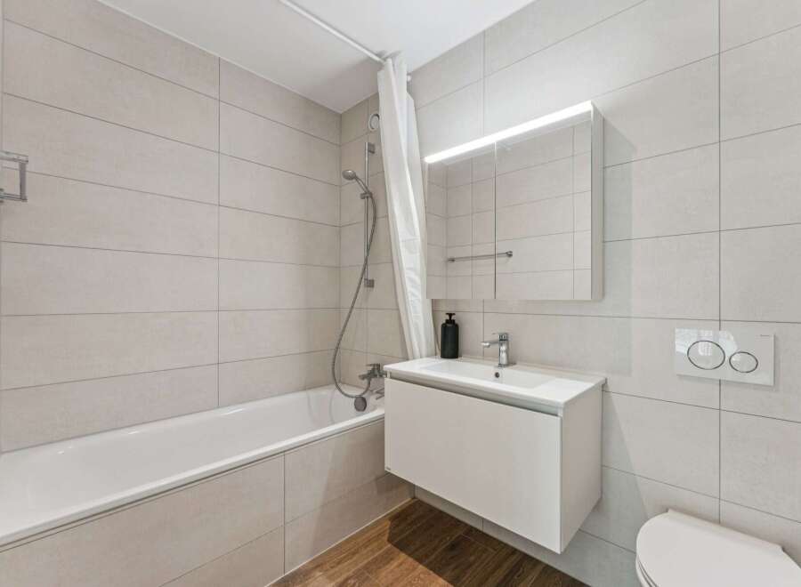 This modern bathroom features a sleek white bathtub with a shower curtain, complemented by light grey tiled walls.