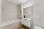 This modern bathroom features a sleek white bathtub with a shower curtain, complemented by light grey tiled walls.
