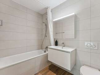 This modern bathroom features a sleek white bathtub with a shower curtain, complemented by light grey tiled walls.