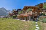 Experience luxurious alpine living in this stunning wooden chalet, featuring expansive balconies with intricate railings and breathtaking mountain views.