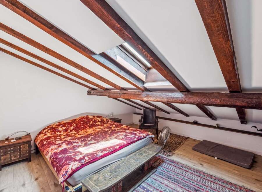Discover this charming attic bedroom featuring exposed wooden beams and a skylight that floods the space with natural light.