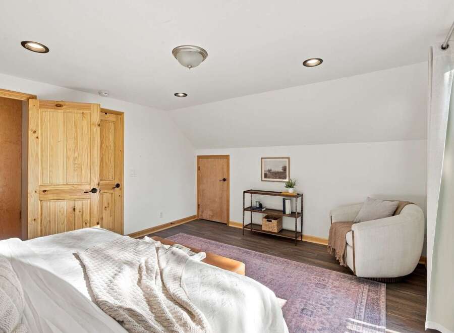 Discover this charming bedroom featuring a cozy reading nook with a comfortable armchair and a stylish shelving unit.