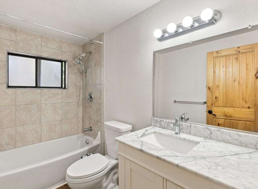 This beautifully updated bathroom features a spacious bathtub with a tiled shower surround and a convenient window for natural light.