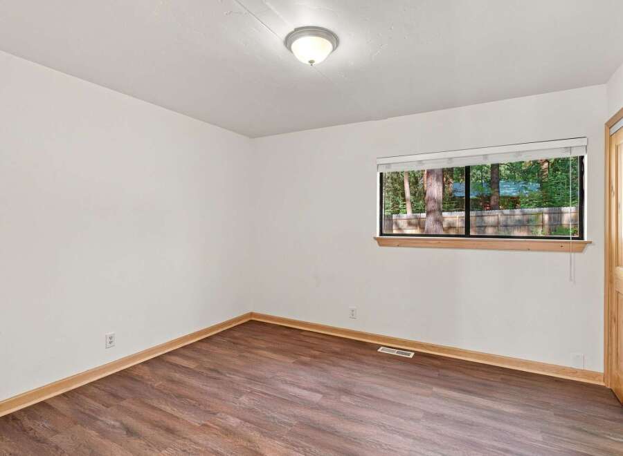 This inviting room features a large window offering serene views of the surrounding trees and a wooden fence.