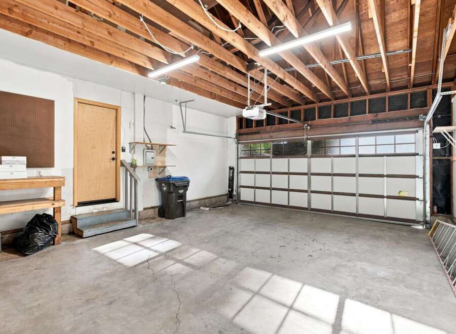 This spacious garage offers ample room for vehicles and storage, featuring a durable concrete floor and exposed wooden beam ceiling.