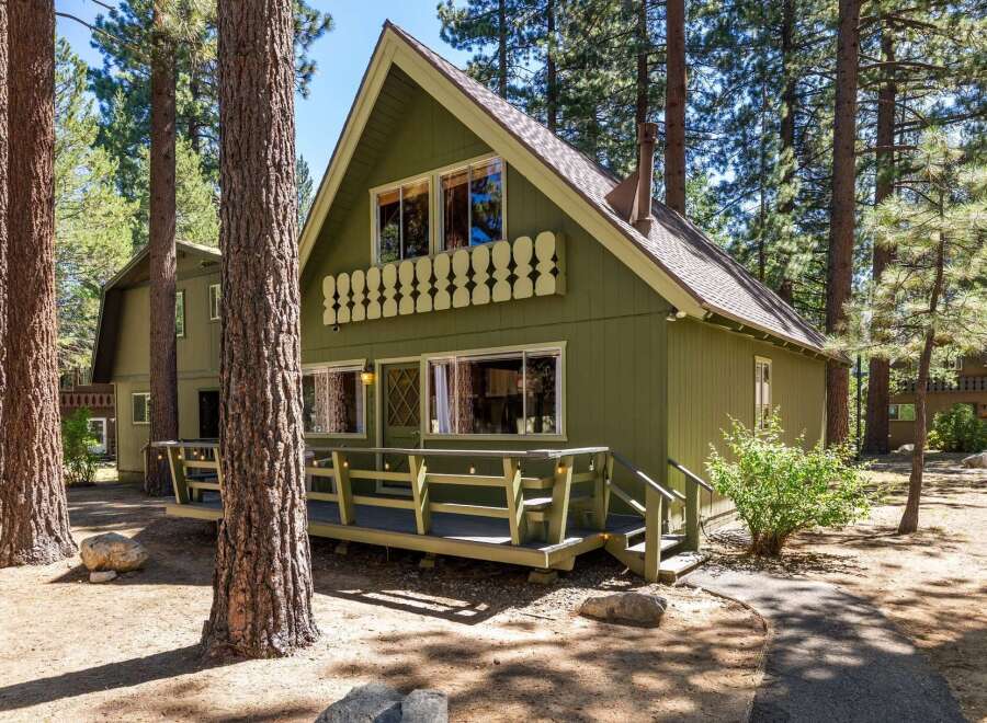Nestled amongst tall pine trees, this charming green cabin offers a serene mountain retreat.