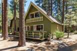 Nestled amongst tall pine trees, this charming green cabin offers a serene mountain retreat.