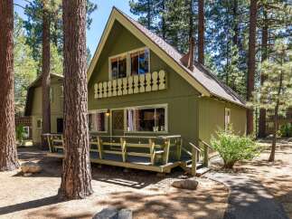 Nestled amongst tall pine trees, this charming green cabin offers a serene mountain retreat.