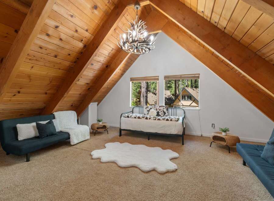 Experience rustic charm in this unique attic bedroom, featuring a stunning antler chandelier and exposed wooden beams that create a cozy, cabin-like atmosphere.