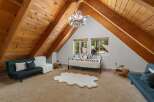 Experience rustic charm in this unique attic bedroom, featuring a stunning antler chandelier and exposed wooden beams that create a cozy, cabin-like atmosphere.