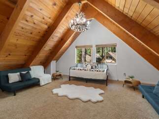 Experience rustic charm in this unique attic bedroom, featuring a stunning antler chandelier and exposed wooden beams that create a cozy, cabin-like atmosphere.