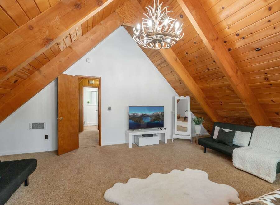 Discover this charming attic living space, featuring a rustic wood-beamed ceiling and a unique antler chandelier that adds a touch of whimsical elegance.
