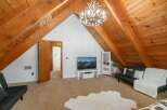 Discover this charming attic living space, featuring a rustic wood-beamed ceiling and a unique antler chandelier that adds a touch of whimsical elegance.