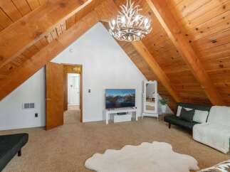 Discover this charming attic living space, featuring a rustic wood-beamed ceiling and a unique antler chandelier that adds a touch of whimsical elegance.