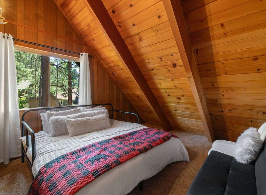 Experience cozy cabin living in this charming bedroom featuring a comfortable bed adorned with a rustic plaid blanket and plush pillows.