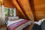Experience cozy cabin living in this charming bedroom featuring a comfortable bed adorned with a rustic plaid blanket and plush pillows.