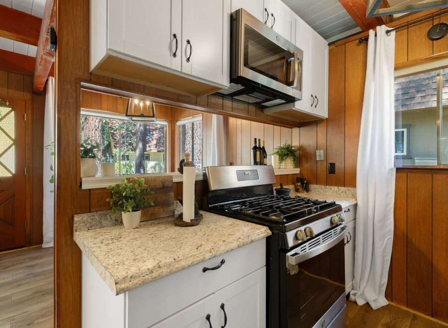 This charming kitchen features a stainless steel gas range and microwave, complemented by white cabinetry and granite countertops.