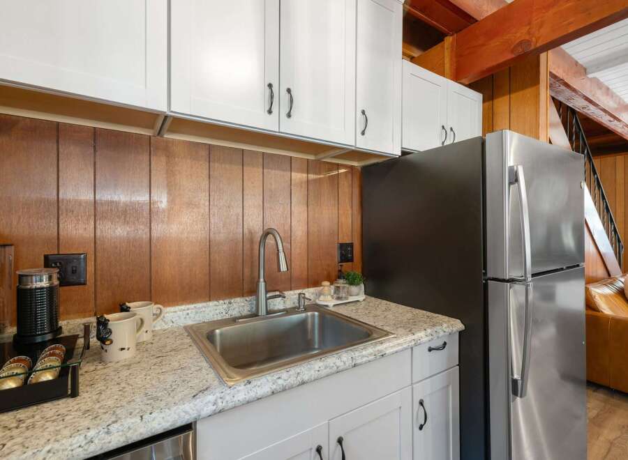 Discover this charming kitchen featuring a sleek stainless steel sink and faucet, complemented by warm wood paneling and modern white cabinetry.