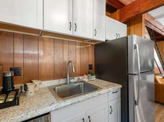 Discover this charming kitchen featuring a sleek stainless steel sink and faucet, complemented by warm wood paneling and modern white cabinetry.