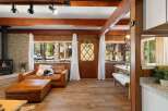 Experience cozy living in this charming cabin-style home, featuring a warm leather sofa and ottoman perfect for relaxing by the fireplace.