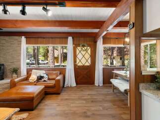 Experience cozy living in this charming cabin-style home, featuring a warm leather sofa and ottoman perfect for relaxing by the fireplace.