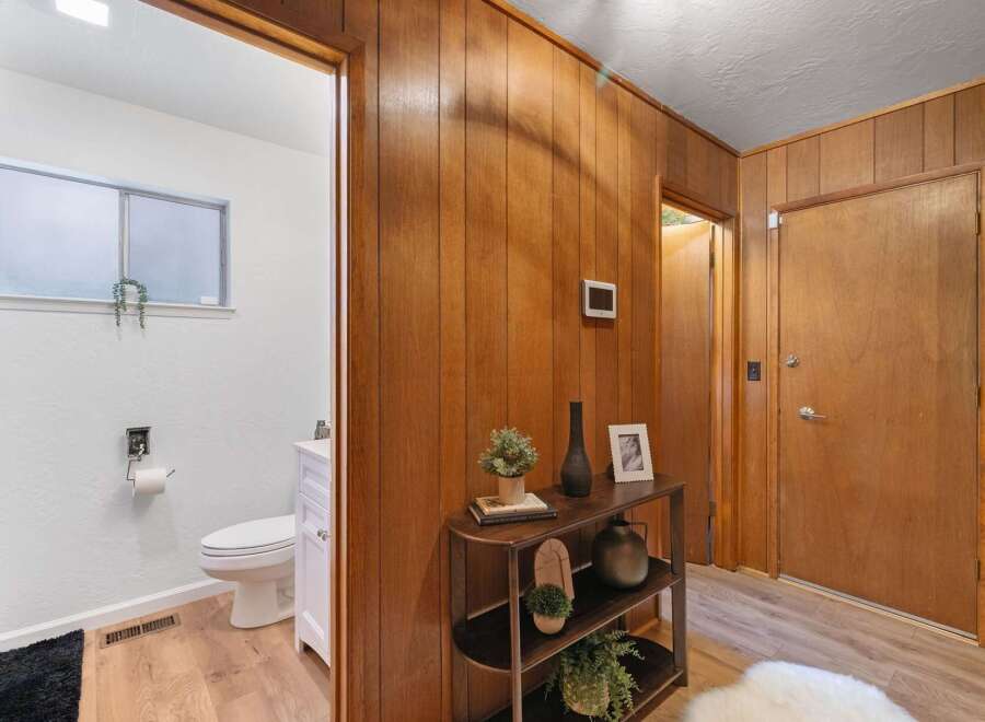 Step into a charming entryway featuring warm wood paneling and a convenient doorway leading to a bright, white bathroom.